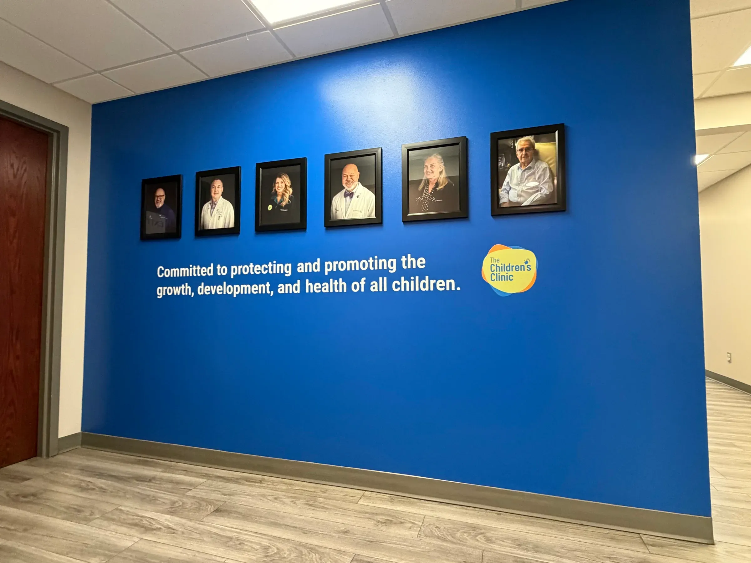 A blue wall of framed physician portraits above the clinic mission statement and logo